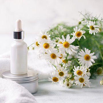 Organic vegan natural cosmetics concept. Chamomile flowers and cosmetic bottles of cream and serum essential on white background. Zero waste cosmetic package