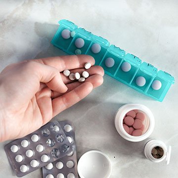 Hand with pills and pillbox. Top view of seven day pill box with pills. Green pill-box over light marble table. Open pill box and open boxes with pills or vitamins. Copy space. Top view or flat-lay.